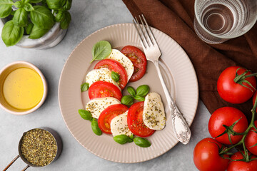 Delicious Caprese salad with tomatoes, mozzarella, basil and spices served on light grey table, flat lay