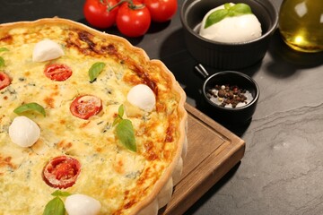 Delicious homemade cheese quiche and ingredients on black table, closeup