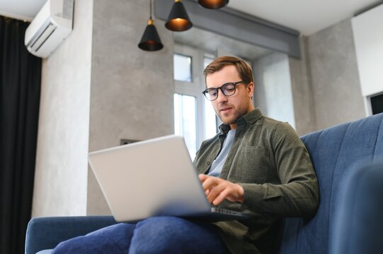 Young cheerful man sitting on sofa with laptop