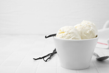 Delicious vanilla ice cream in bowl on white tiled table, closeup. Space for text