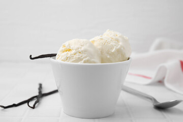 Delicious vanilla ice cream in bowl on white tiled table, closeup
