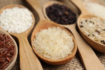 Spoons with different sorts of rice on burlap fabric, closeup