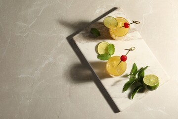 Glasses of tasty pineapple cocktail decorated with cherry and lime on light grey marble table, top view. Space for text