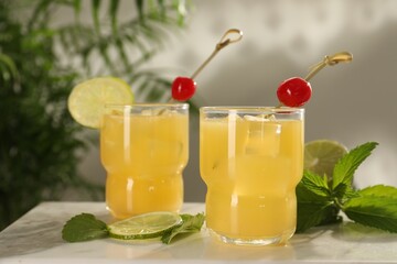 Glasses of tasty pineapple cocktail with cherry, lime and mint on white table