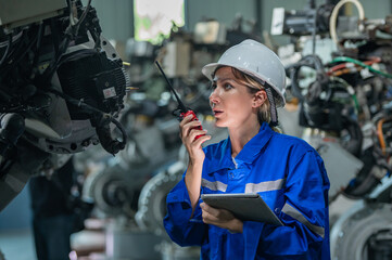 Fototapeta na wymiar woman engineer in uniform helmet inspection check control heavy machine robot arm construction installation in industrial factory. technician worker check for repair maintenance electronic operation