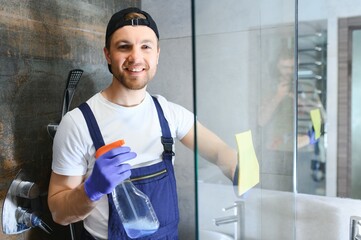 Young caucasian man in uniform cleaning a bath with steam cleaner. Cleaning service concept. Male...