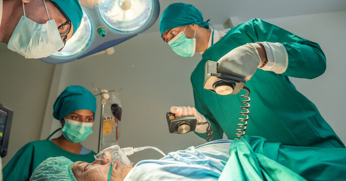 Team of surgery doctor using defibrillator pump chest heart patient to save life while medical surgery in operating room at emergency CPR. Defibrillator in surgeon specialist hand.