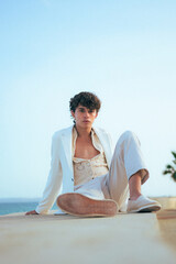 Fototapeta na wymiar Young fashionable man poses in white clothes with the sea on the background