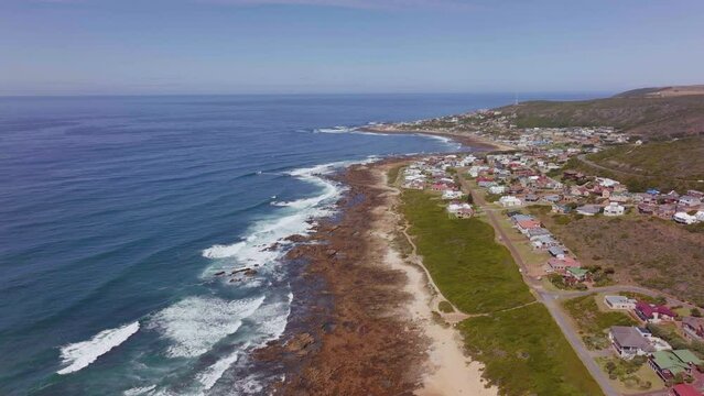 Still Bay aerial drone cinematic beach small surf town Garden Route South Africa Jeffreys Bay homes and buildings waves crashing on reef late morning afternoon forward movement