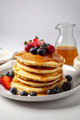 A mouthwatering stack of pancakes topped with maple syrup, blueberries, and strawberries, creating a delightful and indulgent breakfast treat.