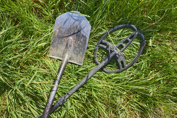 A metal detector and a shovel for searching for coins and precious metal products lie crossed on...