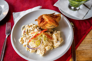 Portion of potato salad with chicken breast, cucumber salad on red table.
