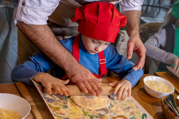 Professional chef teaches boy in chef's costume to cook pizza. Master class. Men's hands close-up.