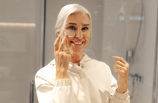 Happy senior woman using an under eye mask in her skincare routine