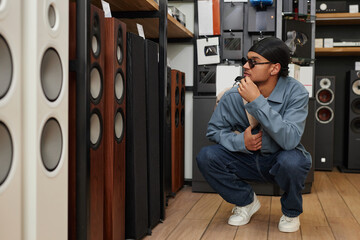 Full length portrait of young black man choosing professional speakers in music store, copy space