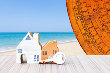 Miniature house with key and old Chinese Feng Shui compass plate over blurred beach background,...