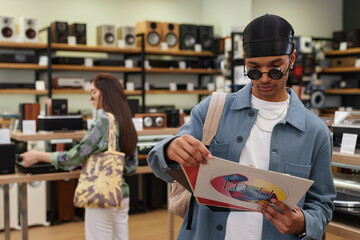 Waist up portrait of black young man holding set of vinyl records in music store, copy space