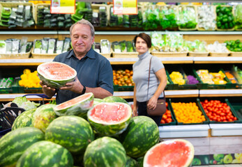 elderly man chooses watermelon in fruit and vegetable section