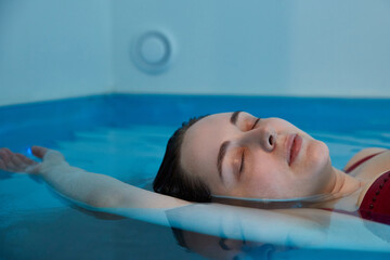 Beautiful woman floating in tank filled with dense salt water used in meditation, therapy, and alternative medicine.