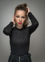 Attractive woman in black blouse and red lips  posing challenging in front of a background. Classic boudoir scene.  Sensual young  woman with long curly hair and black jeans wearing in front of camera