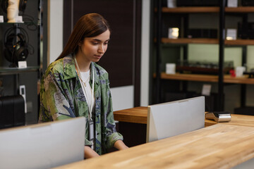 Portrait of young woman working at counter in music store and using computer, copy space