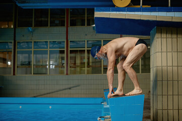 Senior man athlete standing on starting block preparing to jump in pool