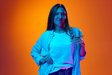 Portrait of young woman in casual clothes posing against gradient orange studio background in neon light