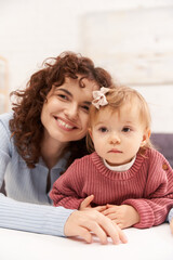 portrait of cheerful woman and child, curly working mother hugging baby girl, balanced lifestyle, bonding, happy family time, modern parenting, joy, engaging with kid, loving motherhood