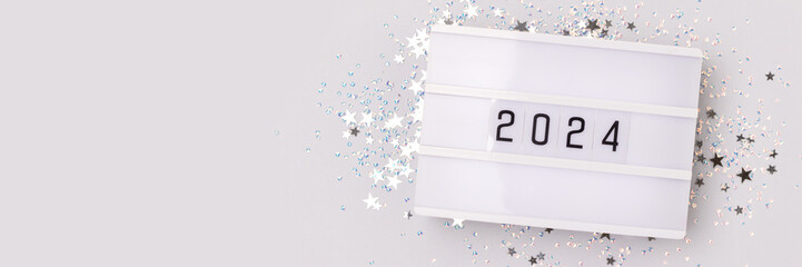 Banner with 2024 numbers and shiny silver stars confetti on a blue background. New Year festive...