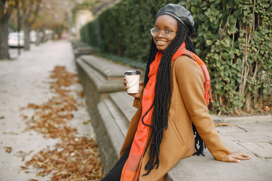 Young black woman in a coat drinking coffee outside