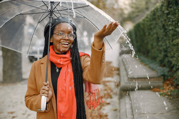 Young black woman in a coat standing under a transparent umbrella outside