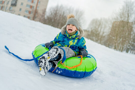 cute caucasian elementary age boy sliding down the slope in park . Winter activities concept. Happy childhood. Image with selective focus.