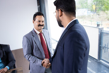 Indian business people handshaking after finishing up a meeting and striking a deal in boardroom.