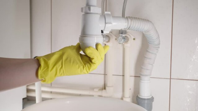 Plumber unscrews the siphon under the sink and cleans the pipes from hair and dirt in the bathroom