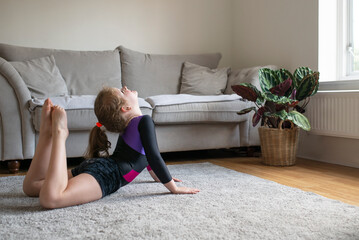 Pretty young girl in gymnastics leotard sportswear doing fitness exercises at home, yoga, stretching