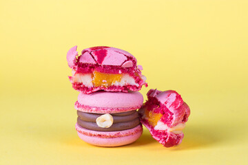 Pink macarons with hazelnuts, caramel and orange filling on bright yellow background