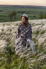 Portrait of a woman in a poncho and a hat. Summer landscape, feather grass field, birches, sky with clouds.