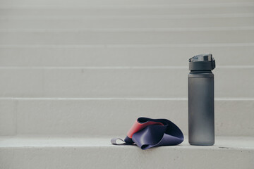 Gray sport bottle drinking water flask and gymnastic elastic bands on white stair. Hydration or...