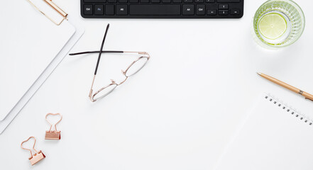 Workplace with white notebook, black keyboard, stationery, glass of water with lime and glasses on white desk. Flat lay office desk, mock up space for text. Top view. Copy space