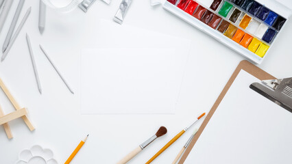 Watercolor, clipboard and other artistic accessories on a white background. Artist's desk workplace. Top view, copy space, flatlay