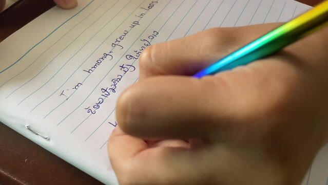 Woman left handed using pen writing English, Lao, Hmong language on white paper.