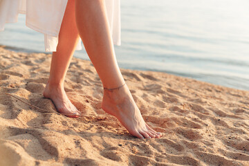 Barefoot woman walking in white dress walking alone on the beach in the sunset