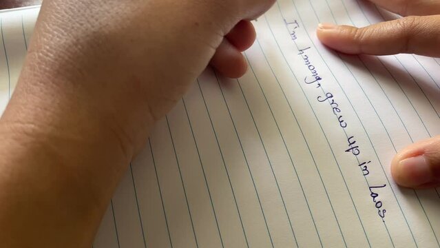 Woman left handed using pen writing English, Lao, Hmong language on white paper.