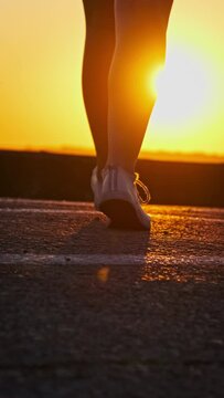 Vertical Silhouette of a girl walking towards the sunset in slow motion. Bottom view of the legs of a slender athletic young woman enjoying life. Mental health concept, lifestyle, freedom, happiness.
