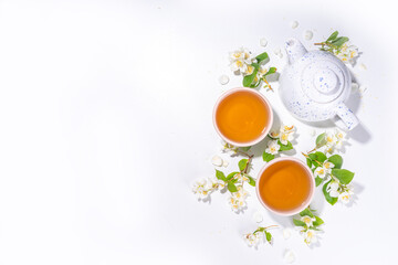 Organic herbal health drink. Jasmine flowers green tea, in white mugs, with teapot, on white table,...