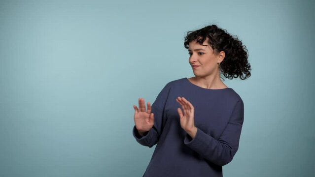 Portrait curly woman need distance showing no stop hands gesture looking at camera. Female wearing blue sweater express no way, no thanks or I don't need it sign on isolated light blue background
