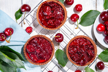 Cherry dessert tartlets. Mini tarts with cream filling and cherry topping, summer traditional pie, with fresh cherries on white wooden background