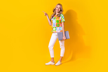 Full length photo of cheerful shiny lady wear flower print t-shirt holding device pointing empty space isolated yellow color background