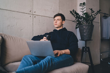 Fototapeta premium Thoughtful young man using netbook while drinking hot beverage