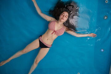 Top view of an attractive young woman floating on blue water. Relaxation and spa therapy. Copy Space